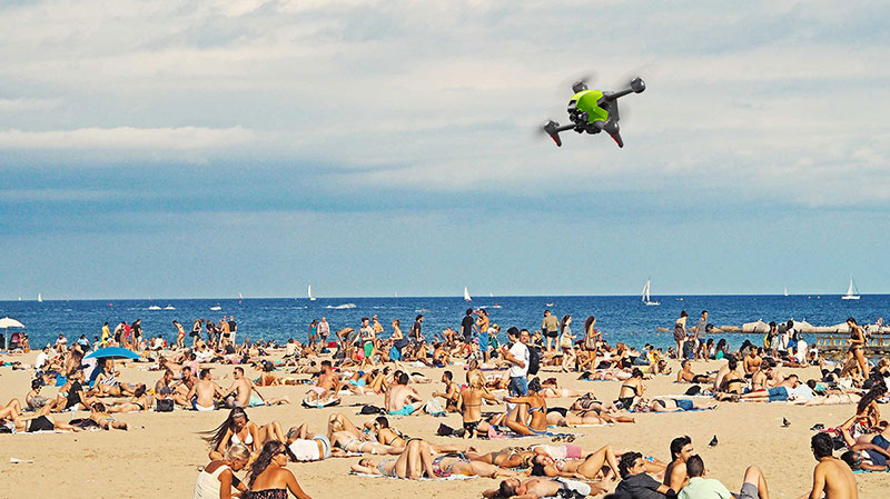 Drone de marque DJI en train de voler au dessus d'une plage et des baigneurs